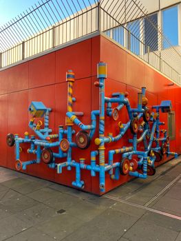 A vibrant urban art installation featuring colorful pipes and wheels on a red wall.