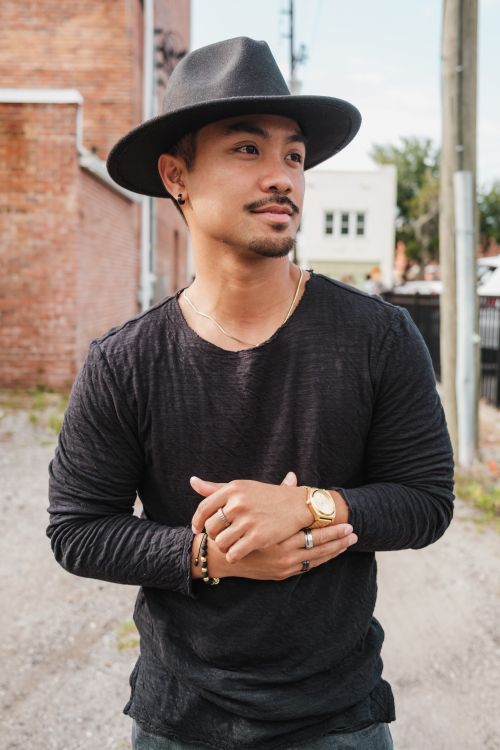 Free Portrait of a fashionable man wearing a black hat and shirt, standing outdoors in an urban setting. Stock Photo
