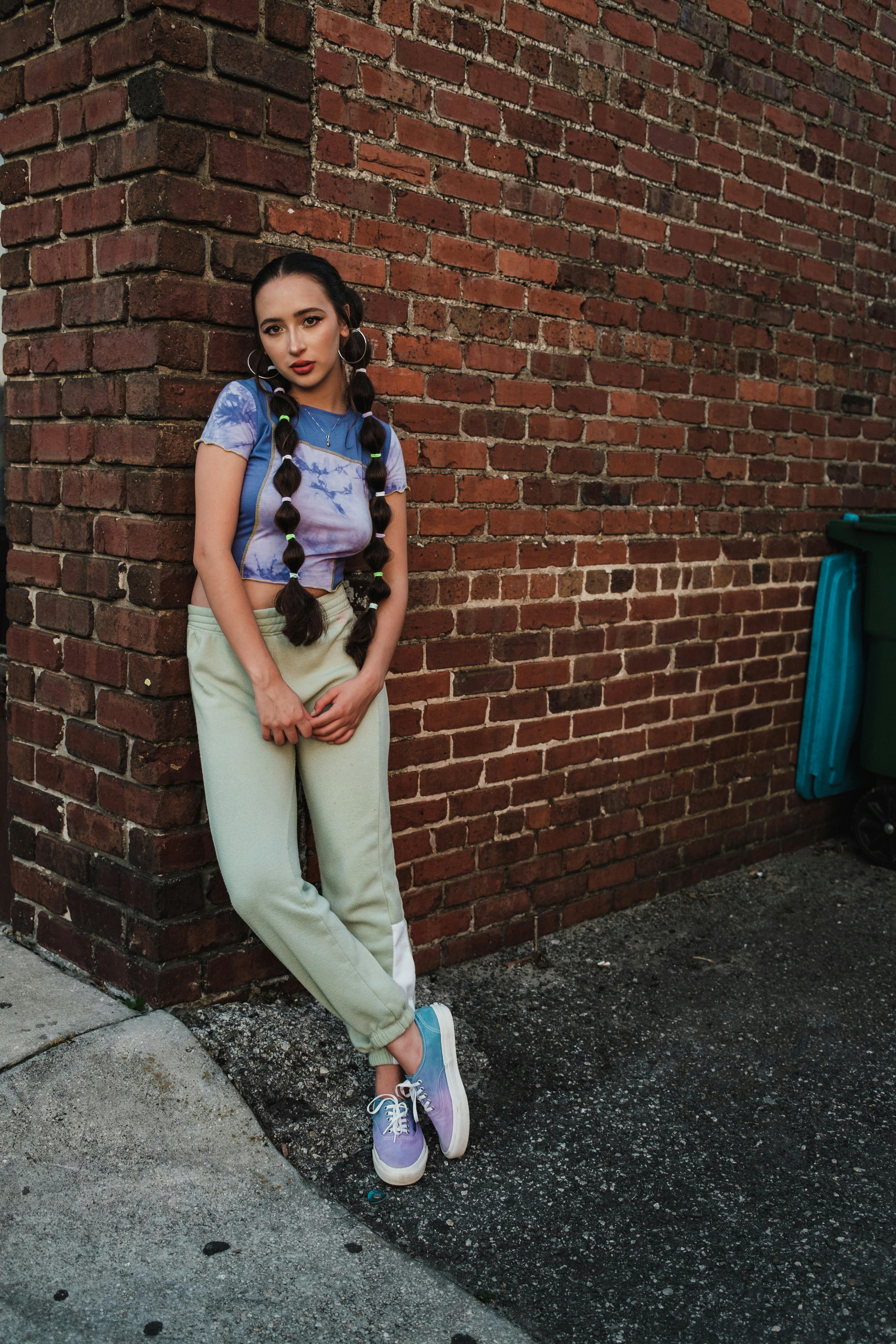 Stylish woman in casual attire posing against a brick wall in a city.