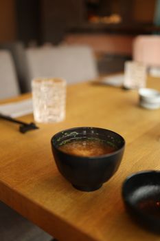 Warm miso soup served in a black bowl on a wooden dining table in a cozy restaurant setting.