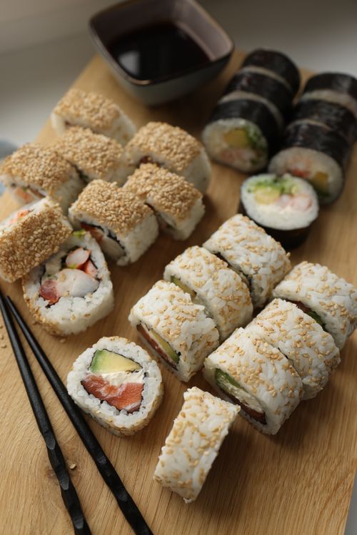 Free An appetizing display of assorted sushi rolls on a wooden board with dipping sauce. Stock Photo