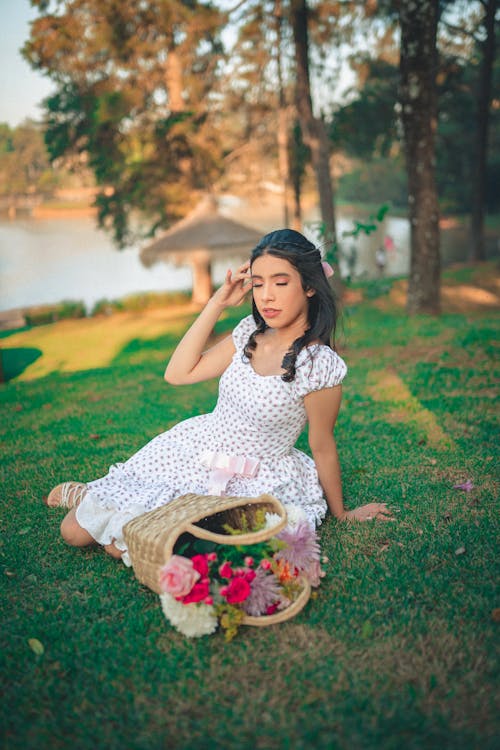 Young Woman Sitting on the Grass in a Park with a Bunch of Flowers in a Basket 