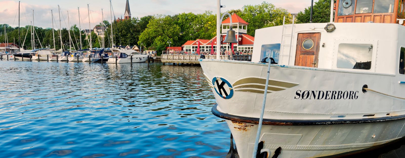 A serene boat scene in Flensburg harbor with vivid reflections and vibrant architecture.