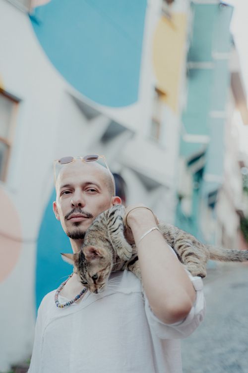 Free A bald man holding a cat on his shoulder against a colorful urban backdrop. Perfect for lifestyle themes. Stock Photo