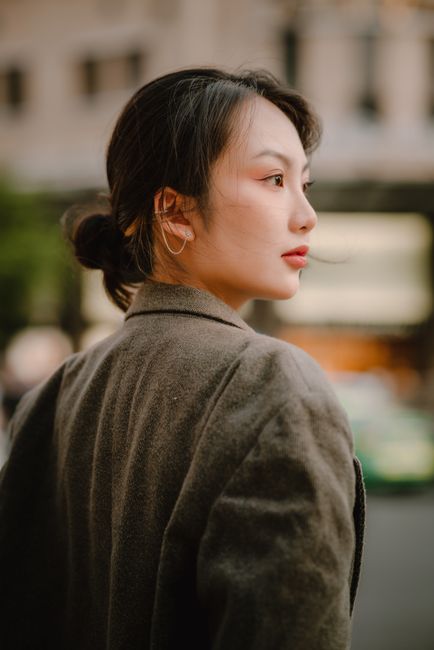 Elegant Asian woman in a coat gazing thoughtfully in an urban setting.