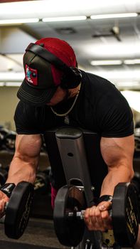 A young muscular man using dumbbells for strength training indoors at a gym.