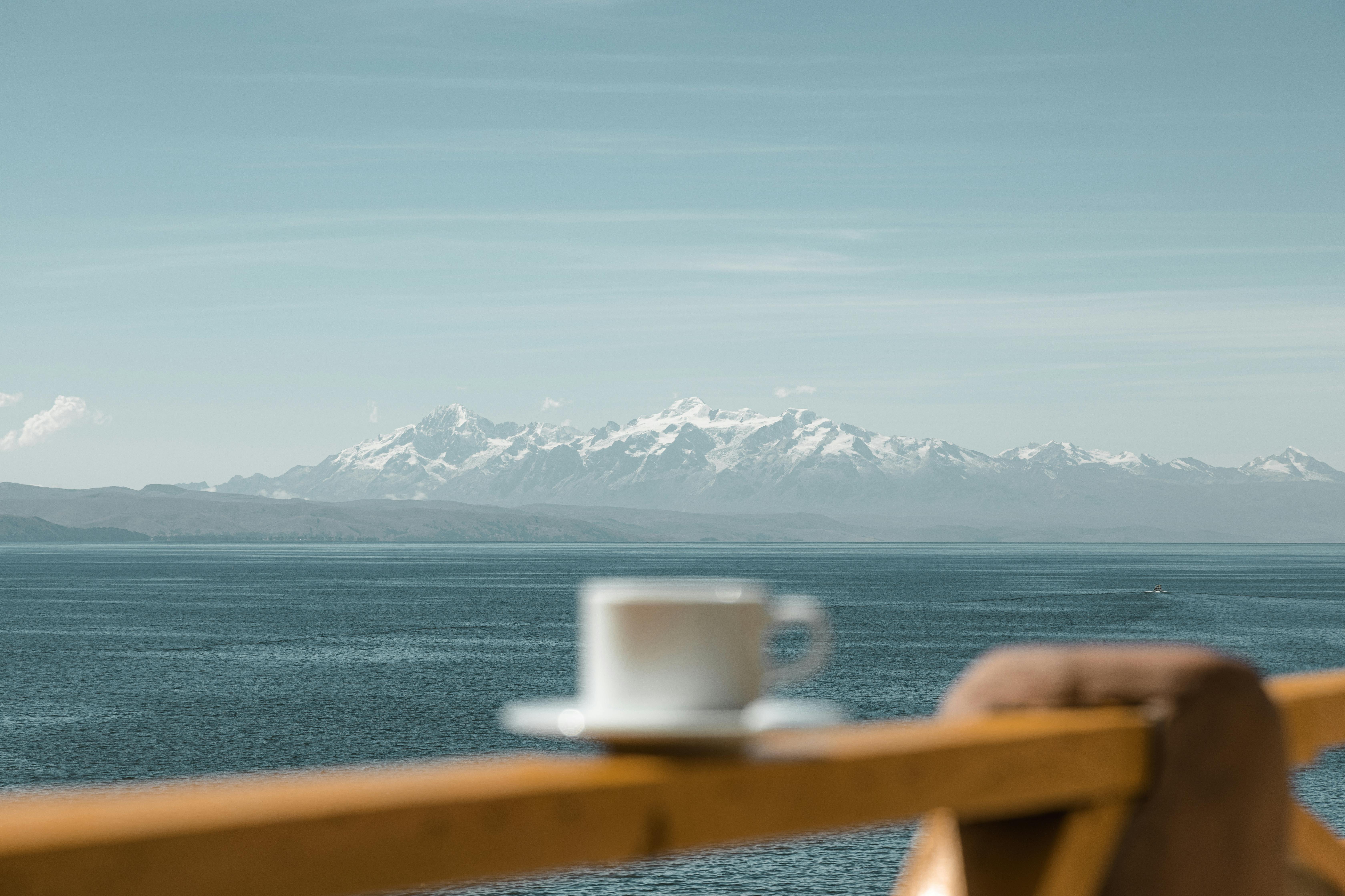 A peaceful scene with mountains, sea, and a cup on a balcony railing.