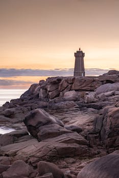 Majestic Ploumanac’h Lighthouse in Brittany, France, framed by rugged rocks and a serene sunset.