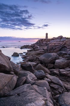 Experience the serene beauty of Phare de Men Ruz lighthouse against dramatic rocky coastline at dusk in Bretagne, France.