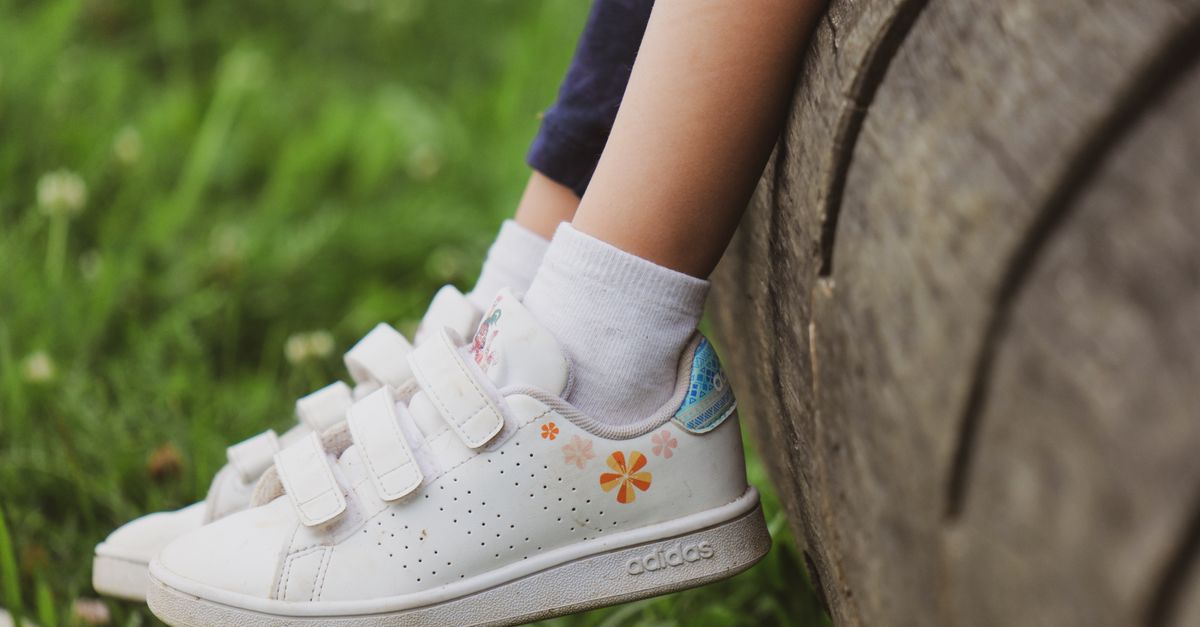 Close-up of a child's feet with sneakers on a log in a grassy meadow, showcasing outdoor play.