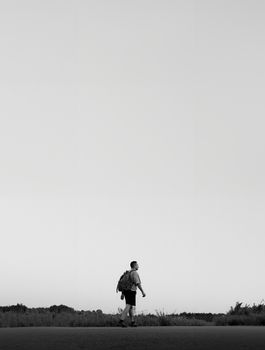 Black and white photo of a lone walker in a minimalistic outdoor setting during evening.
