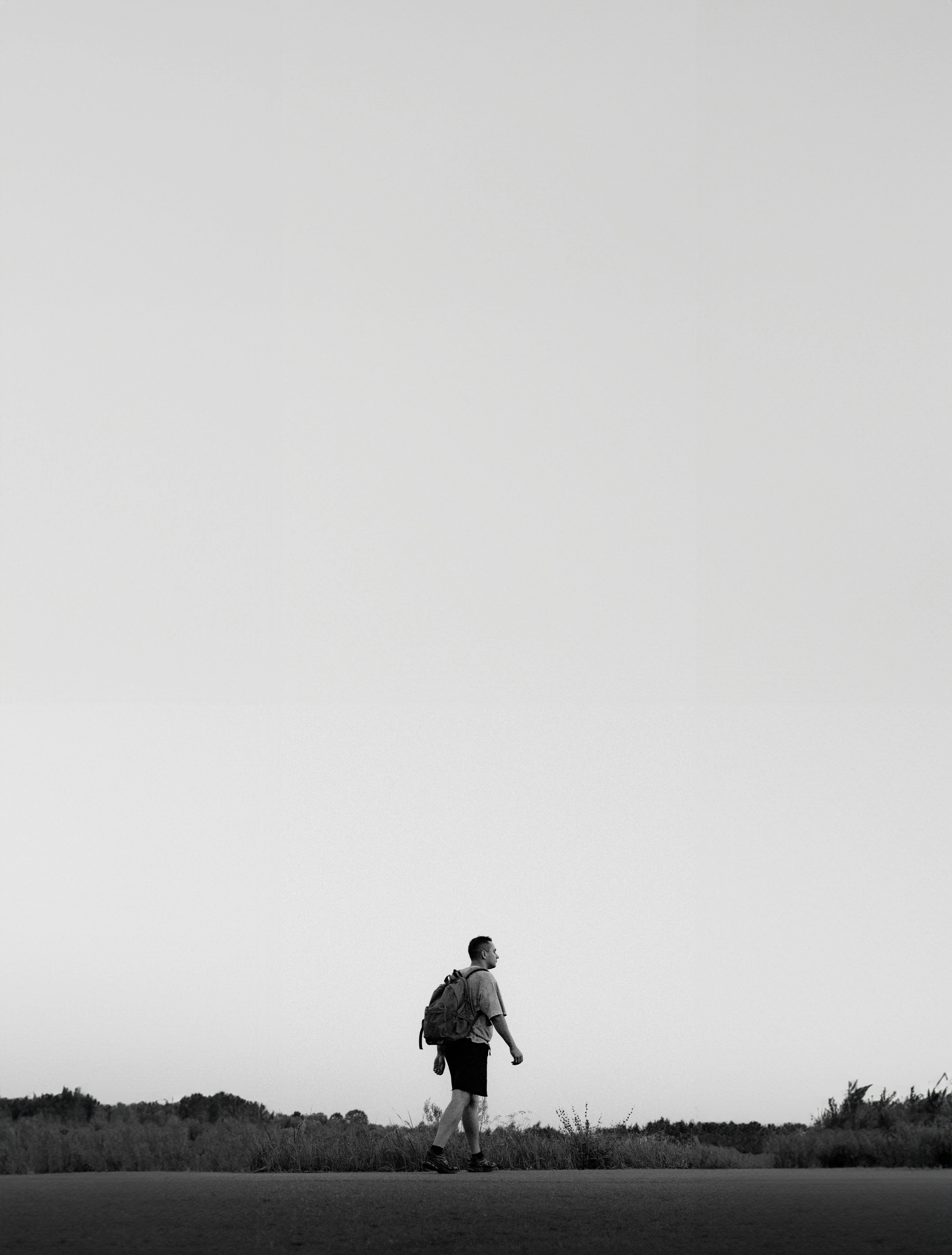 Free Black and white photo of a lone walker in a minimalistic outdoor setting during evening. Stock Photo