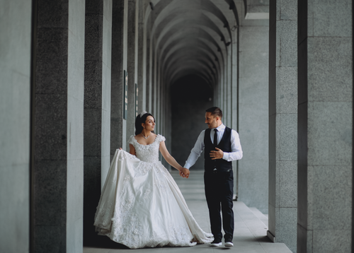 Free Bride and groom walking hand in hand through a majestic colonnade on their wedding day. Stock Photo