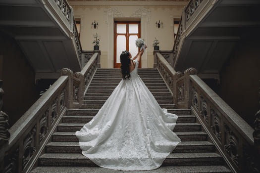 A stunning bride in a wedding dress poses with a bouquet on an elegant staircase.