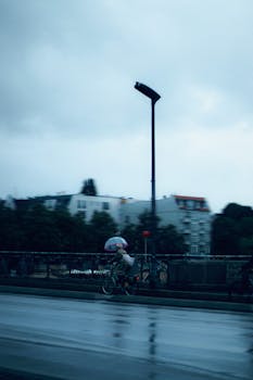 Cyclist with umbrella rides through rain-soaked Berlin street, capturing urban life and weather.