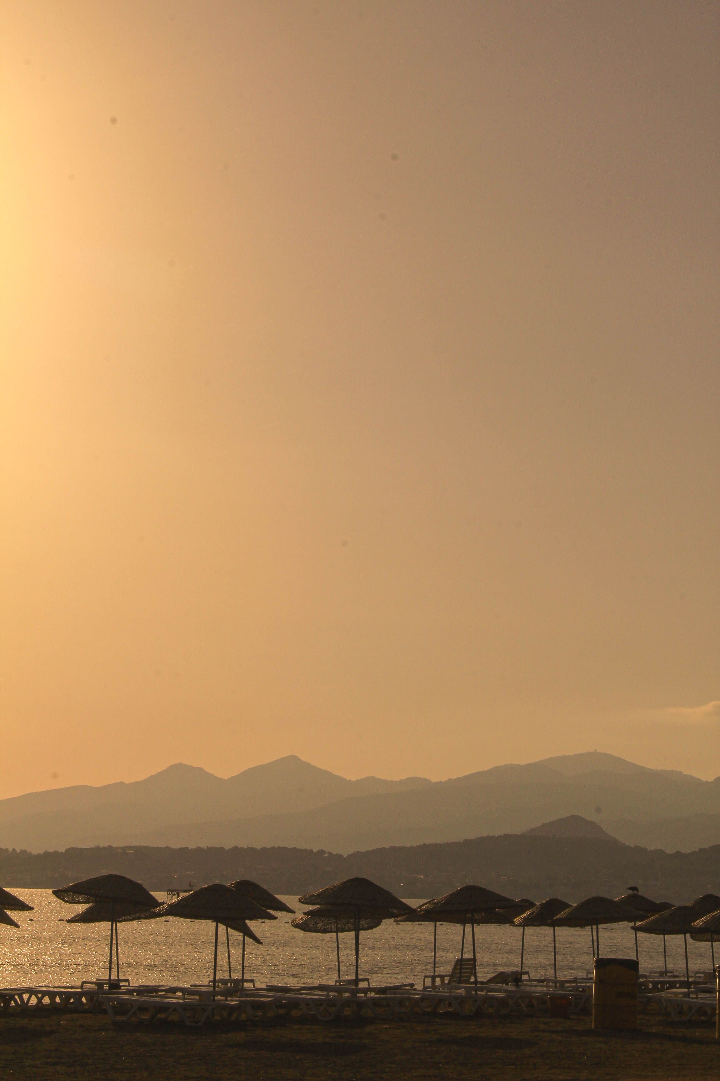 Peaceful sunset scene on a beach with umbrellas and mountains in the background.