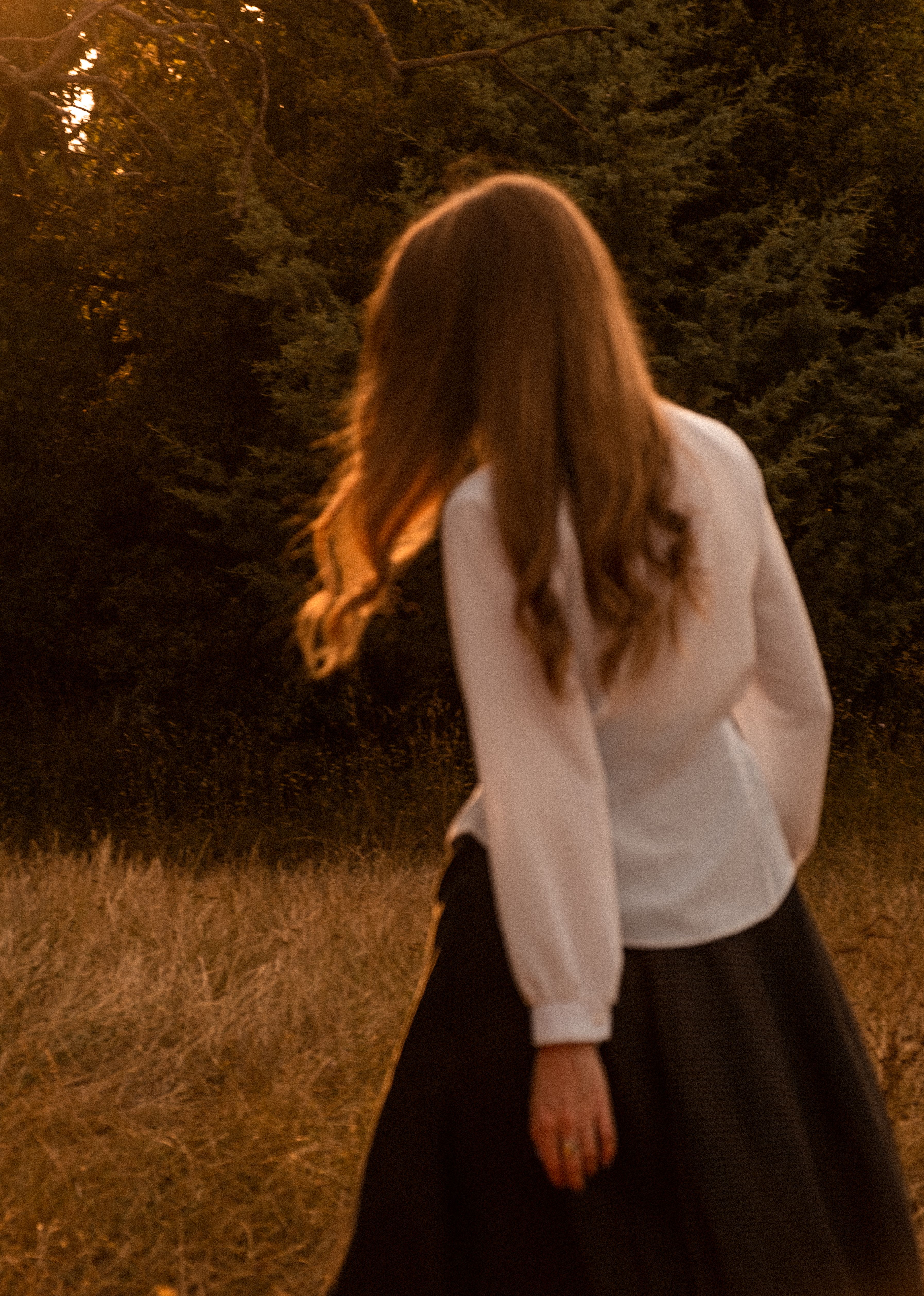 A woman with brown hair walks in a rural grassland during sunset, exuding a serene and natural vibe.