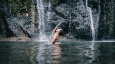 一名女子优雅地在雄伟的瀑布前拂着头发，捕捉到自然与自由的本质