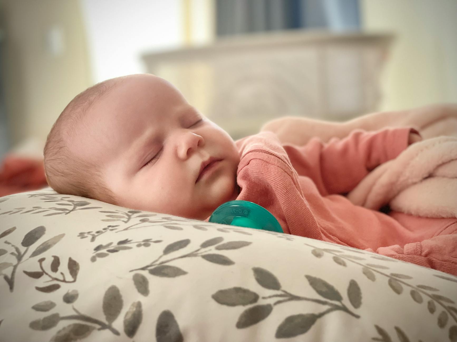 A serene newborn baby sleeping on a patterned pillow indoors, wrapped in a soft blanket.