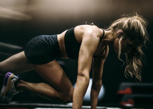 Focused female athlete in active pose working out at a gym in dynamic lighting.