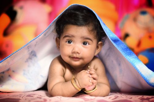 Free Adorable baby under a blue blanket with toys in a studio setting. Stock Photo
