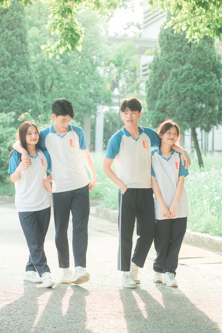 Four Teenager Students In Uniform T-Shirts Posing In A Park