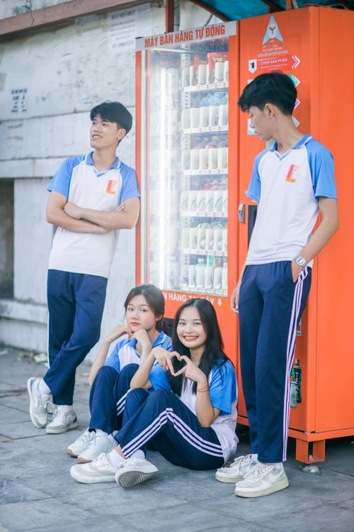Free Group of teenagers in school uniforms posing happily by a vending machine outdoors. Stock Photo