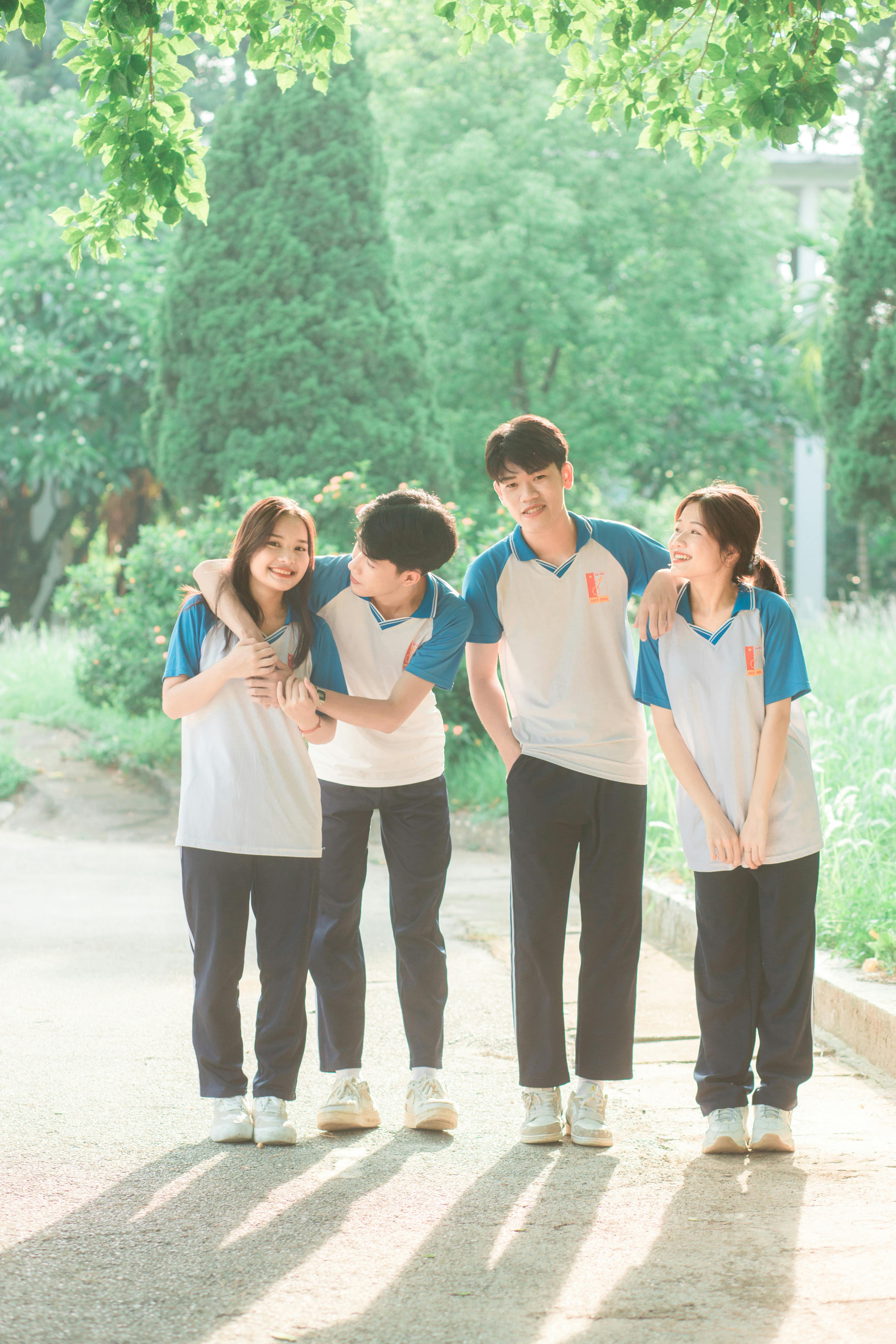 Four teenagers in school uniforms enjoying a sunny day outdoors, smiling and bonding together.