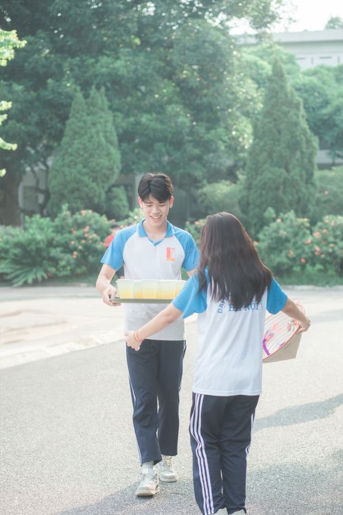 Free Teenagers in uniform smiling and exchanging drinks outdoors on a sunny day. Stock Photo