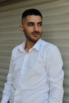 Portrait of a man in a white shirt standing against a shutter door, exuding confidence.