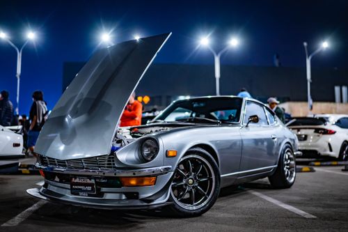 Free A shiny silver classic sports car with its hood open under bright streetlights at a nighttime motor show. Stock Photo