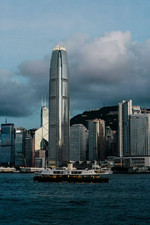 Free Hong Kong cityscape at dusk featuring skyscrapers and a ferry crossing Victoria Harbour. Stock Photo