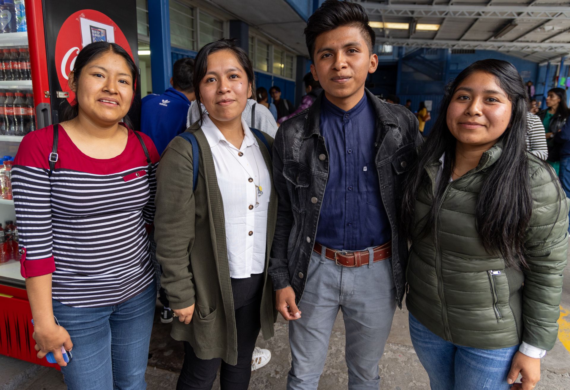 Four young adults standing close together smiling outdoors with a vending machine in the background.