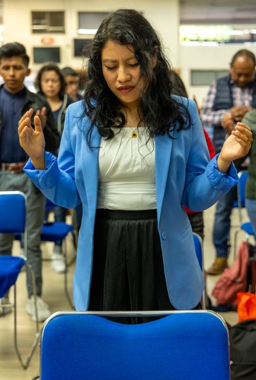 Free A young woman in a blue blazer prays with her eyes closed during a church service, expressing devotion. Stock Photo
