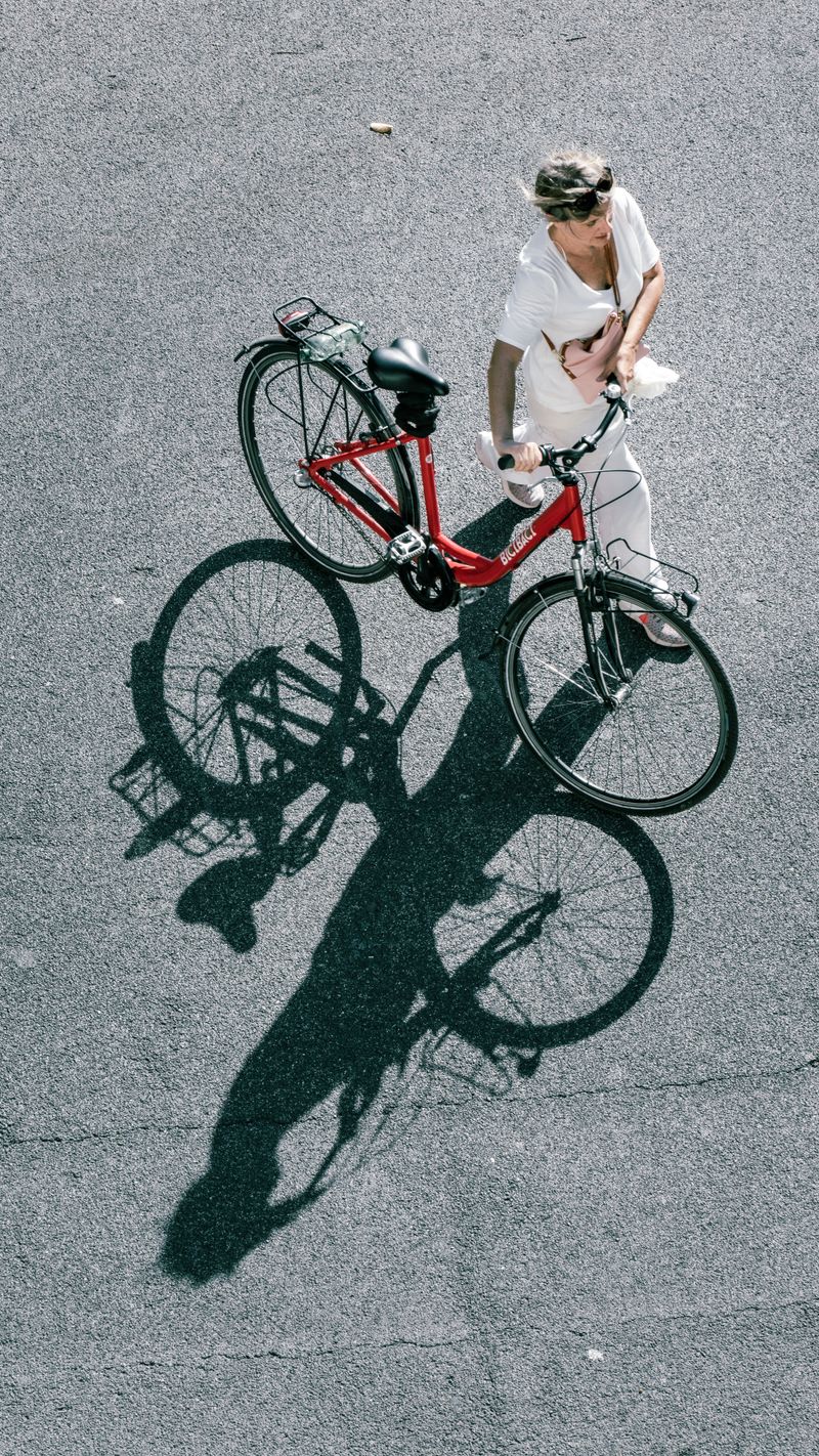 A woman walking her red bicycle on the streets of Rome, casting a distinct shadow.
