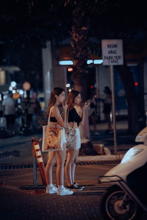 Two Young Women Standing on the Street in City at Night 