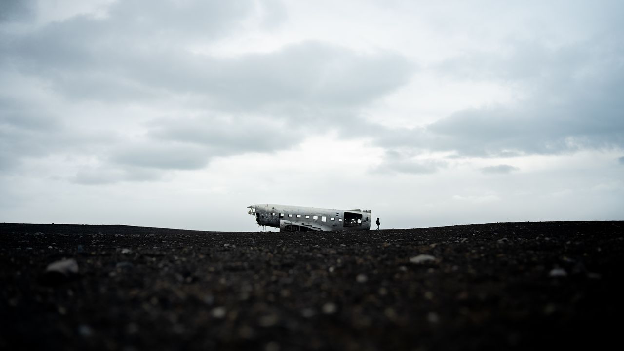 a haunting image of a plane wreck on a barren landscape under a cloudy
