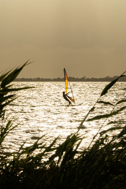 Person windsurfing at sunset on shimmering waters in Wiek, Germany.