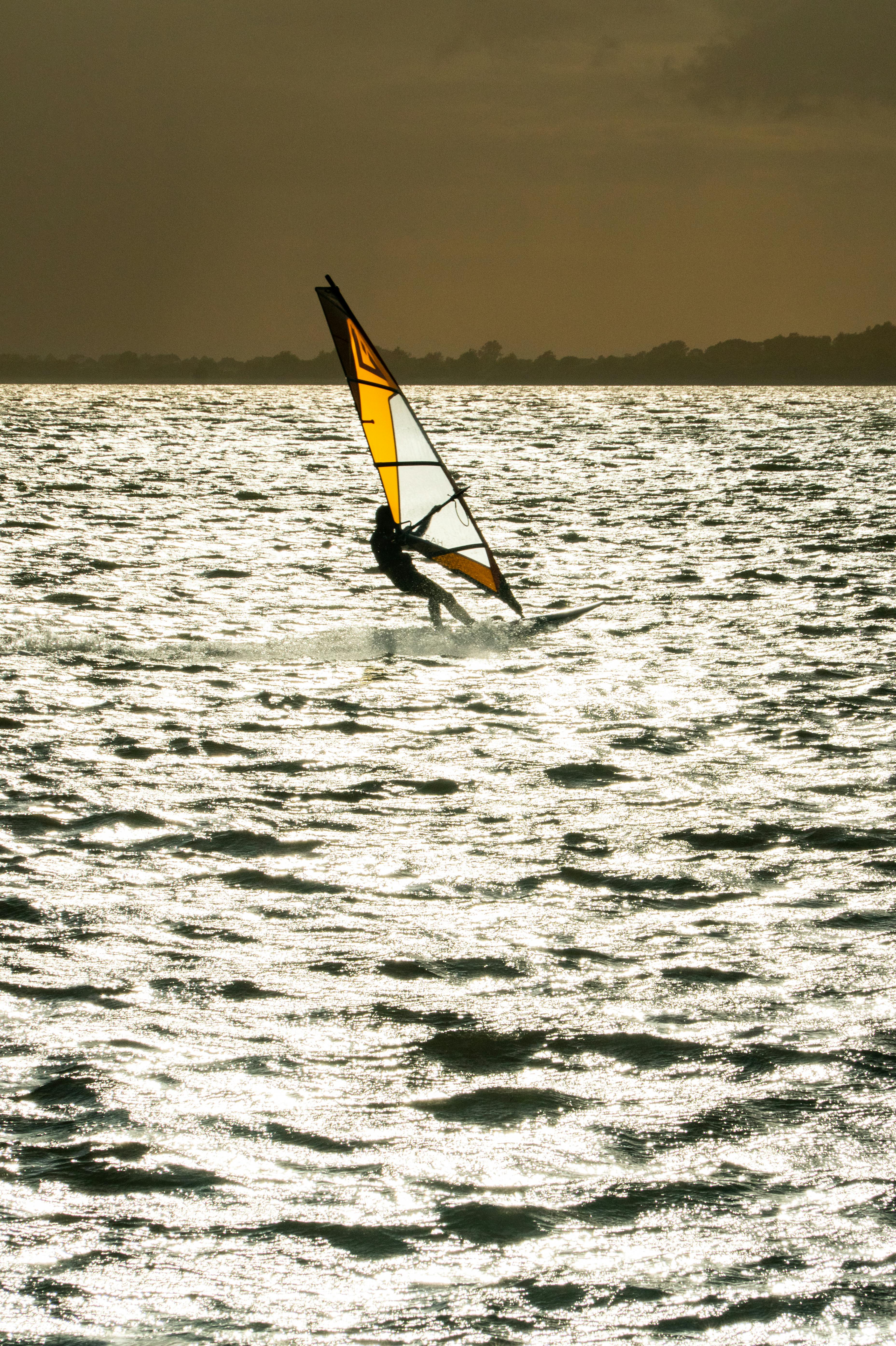 A captivating shot of a windsurfer gliding across the ocean at sunset, highlighting leisure and adventure.