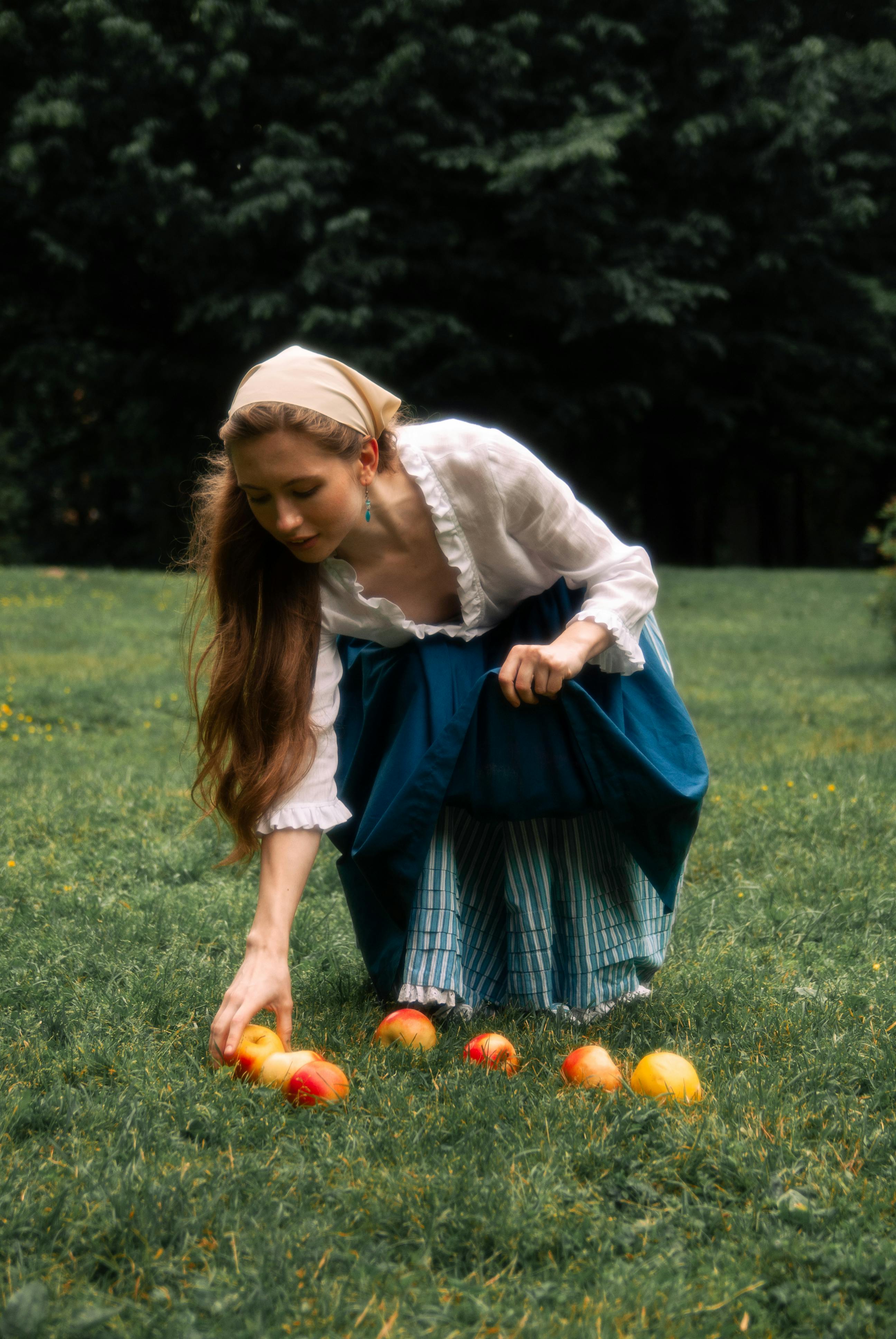 woman in traditional peasant clothing picking apples from grass