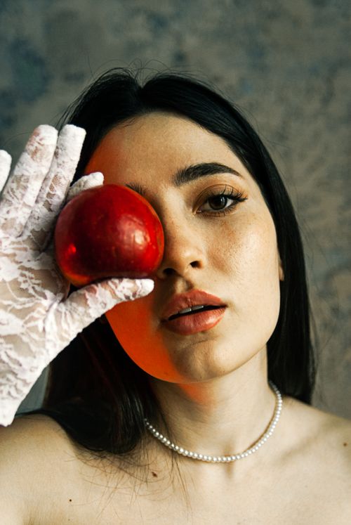Free Portrait of a brunette woman holding a red apple with a lace glove, exuding elegance and mystery. Stock Photo