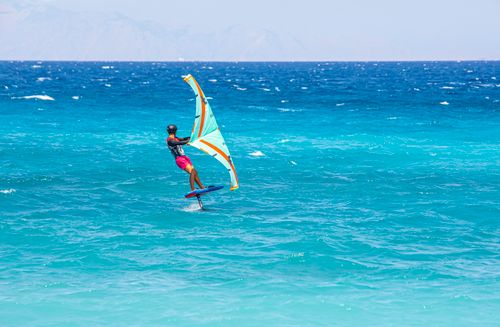 Free A thrilling wind foiling scene with a man gliding over vibrant ocean waves, perfect for adventure seekers. Stock Photo