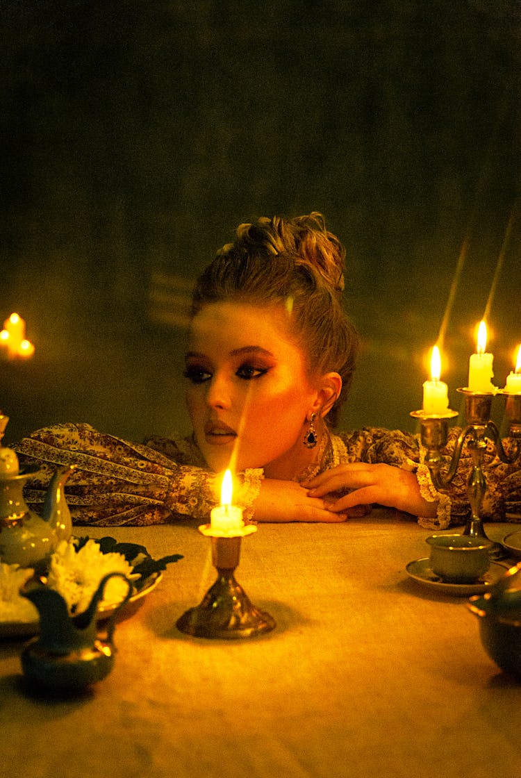 Young Woman In Brocade Dress Sitting By A Table With Burning Candles