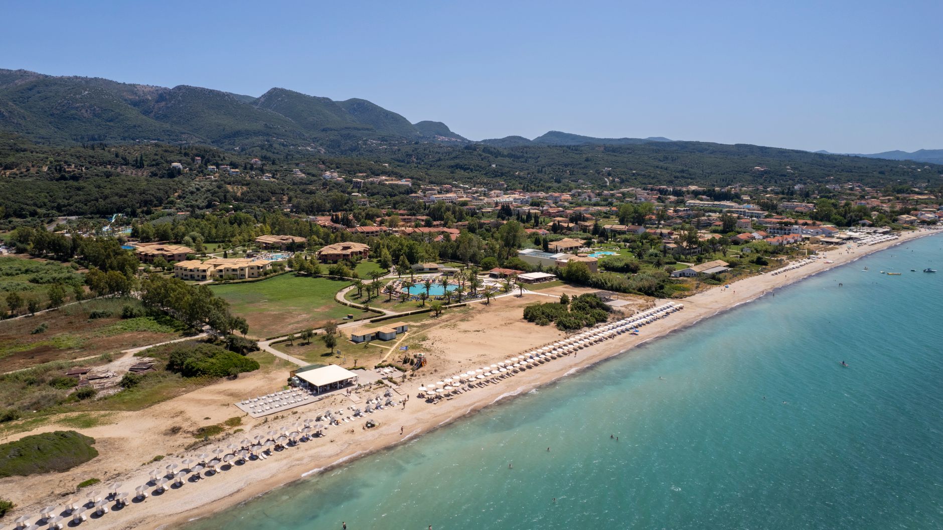 Aerial shot of a coastline resort in Corfu, Greece with a beautiful beach and lush surroundings.