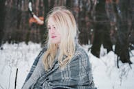 白雪皑皑的冬季森林里，一名围着格子围巾的金发女子，神情平静而沉思