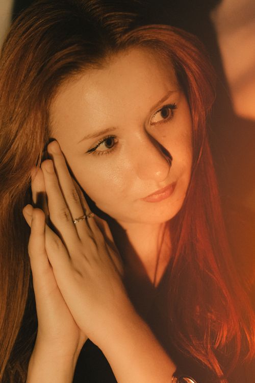 Free Close-up portrait of a woman with folded hands in warm lighting, conveying contemplation. Stock Photo