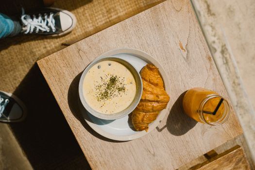 Top view of a breakfast setup with croissant, creamy soup, and orange juice.