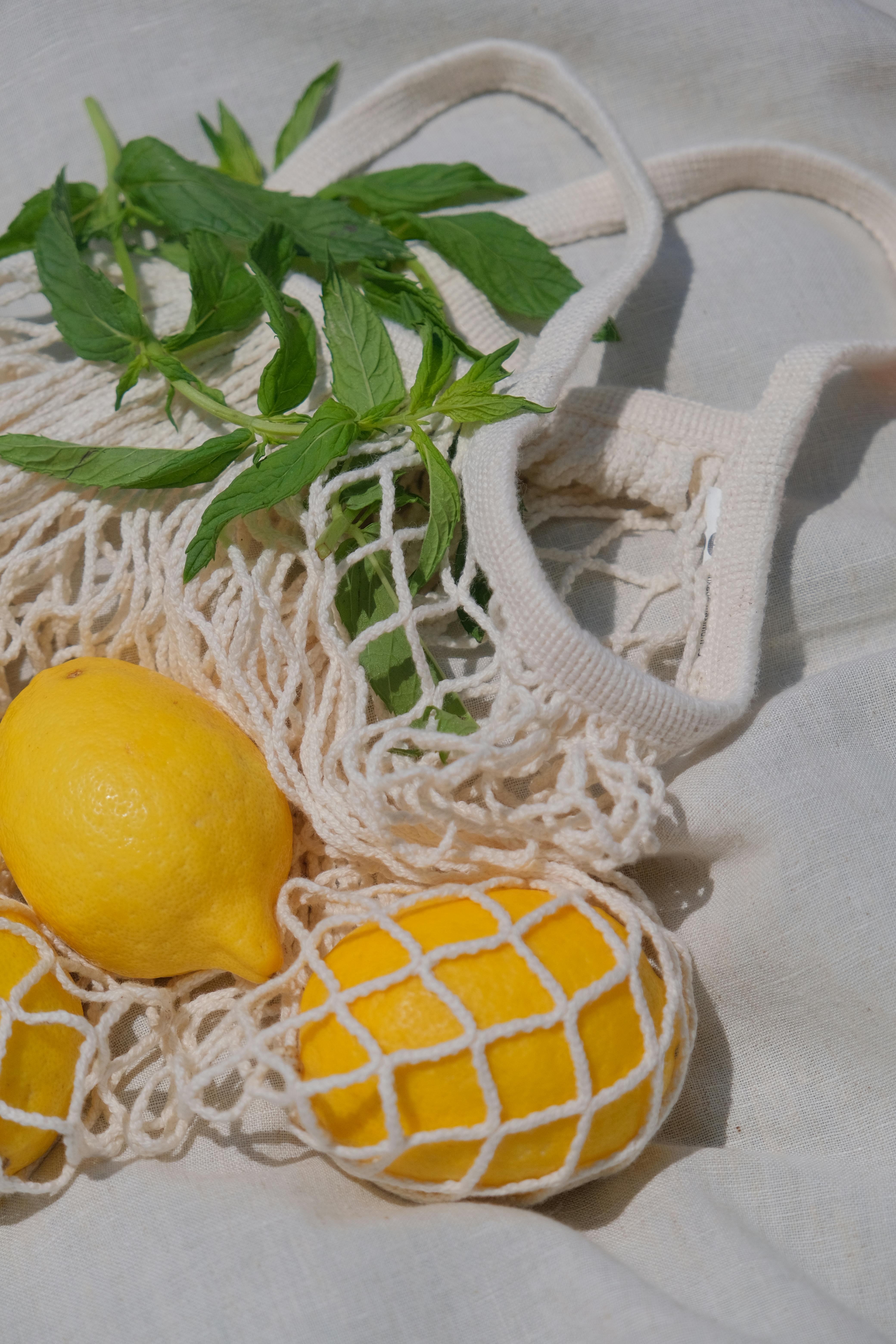 Bright lemons with fresh mint leaves in a reusable net bag for sustainable shopping.