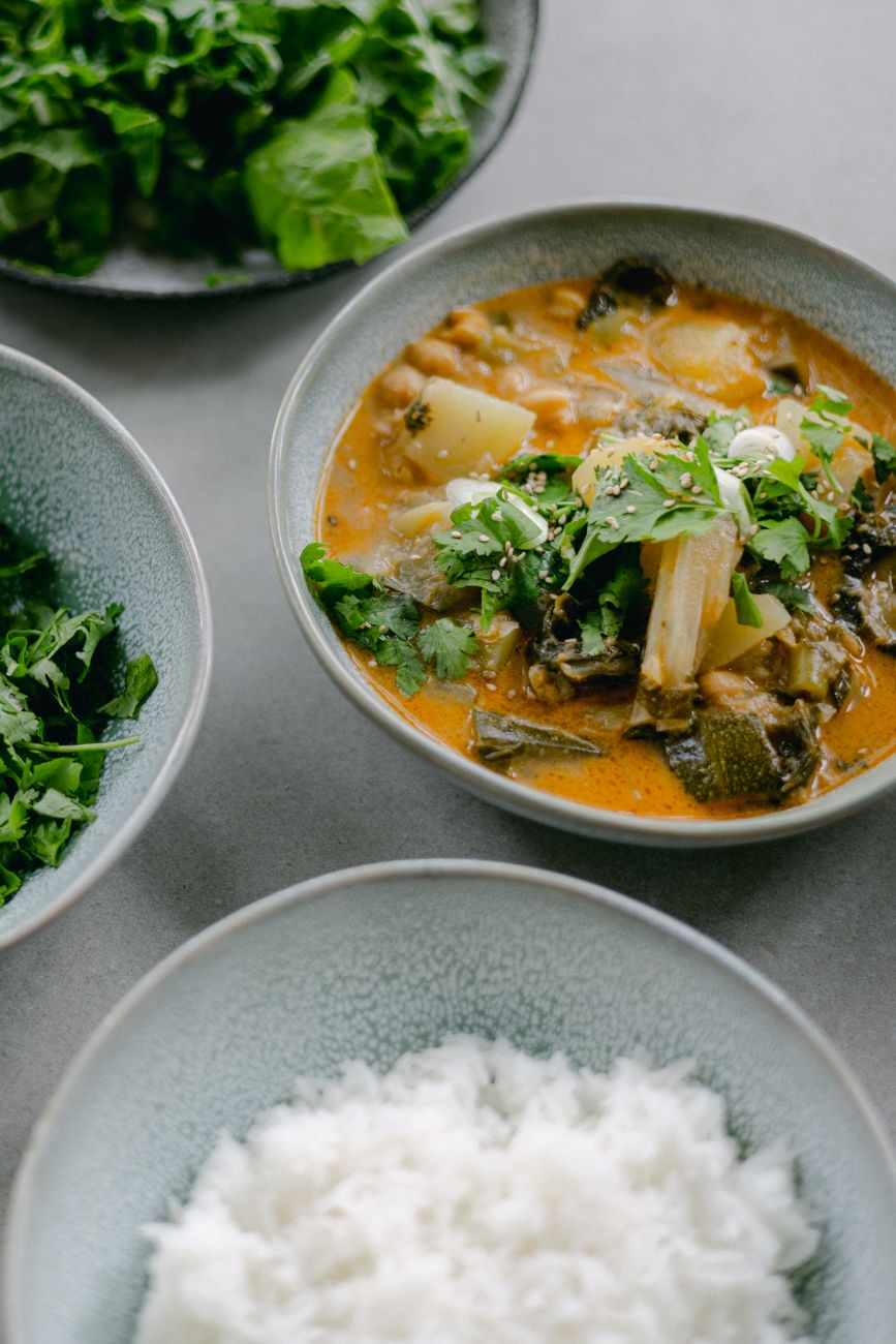 A bowl of rich, golden-brown groundnut stew with chunks of sweet potatoes and dark green collard greens in a creamy peanut sauce