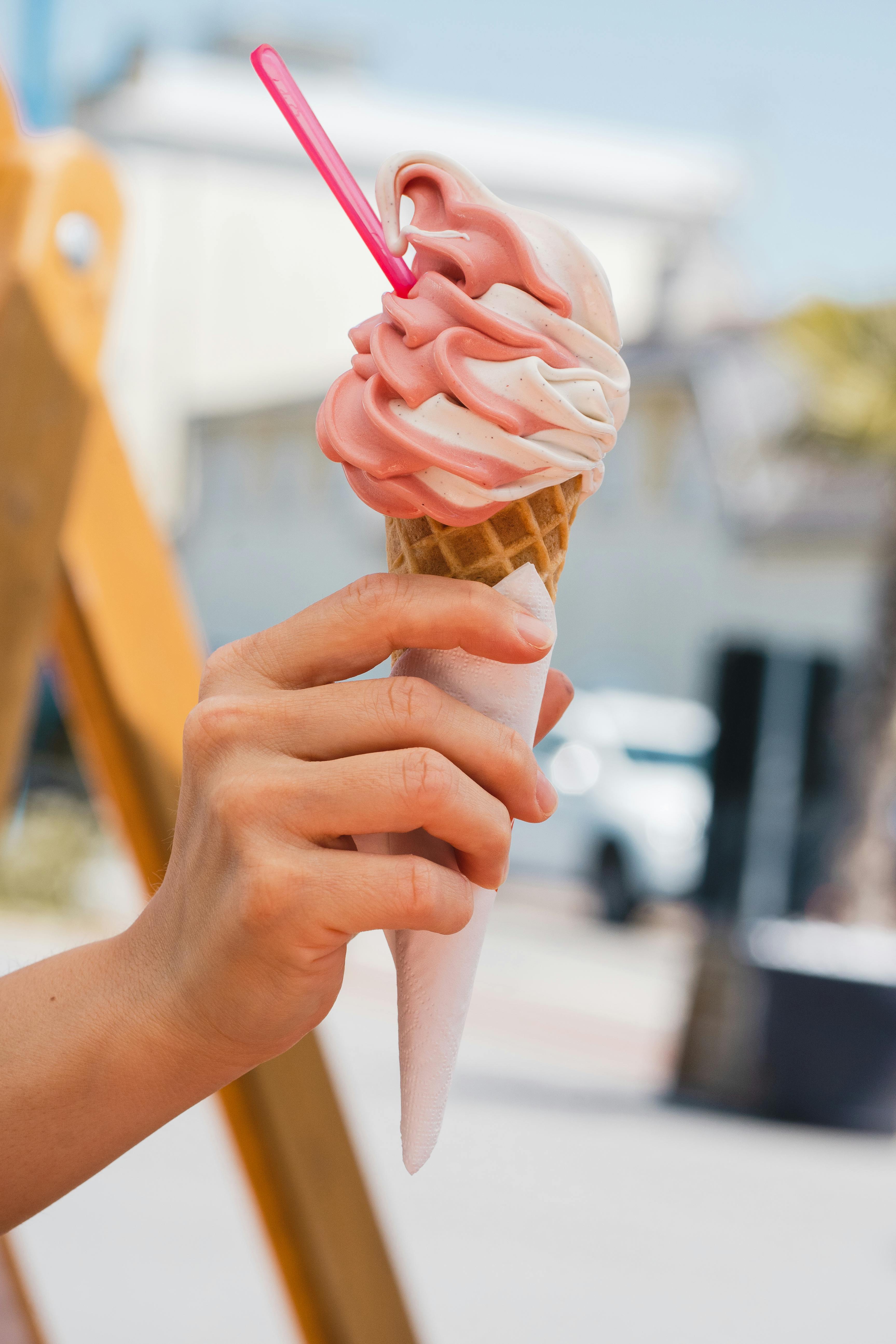 Close-up of a hand holding a strawberry and vanilla ice cream cone outdoors in Pénestin, France.